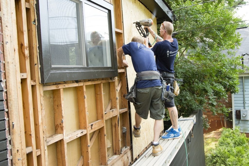 Two men adding wooden exterior siding to a house