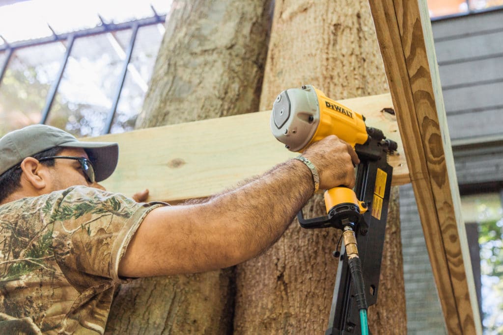 Man with nail gun adding wood frame around trees